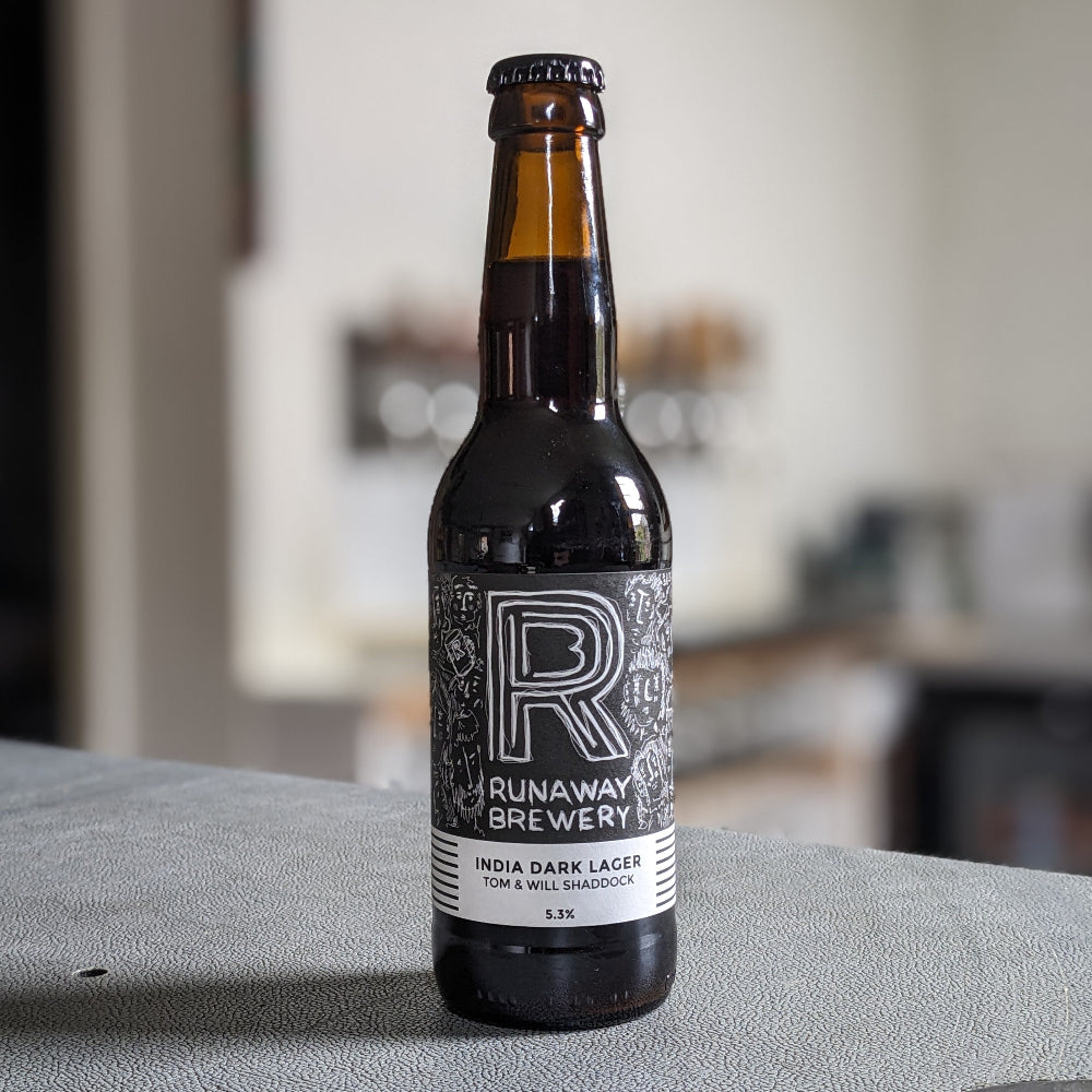 Bottle of Runaway Brewery India Dark Lager on a table with a blurred background